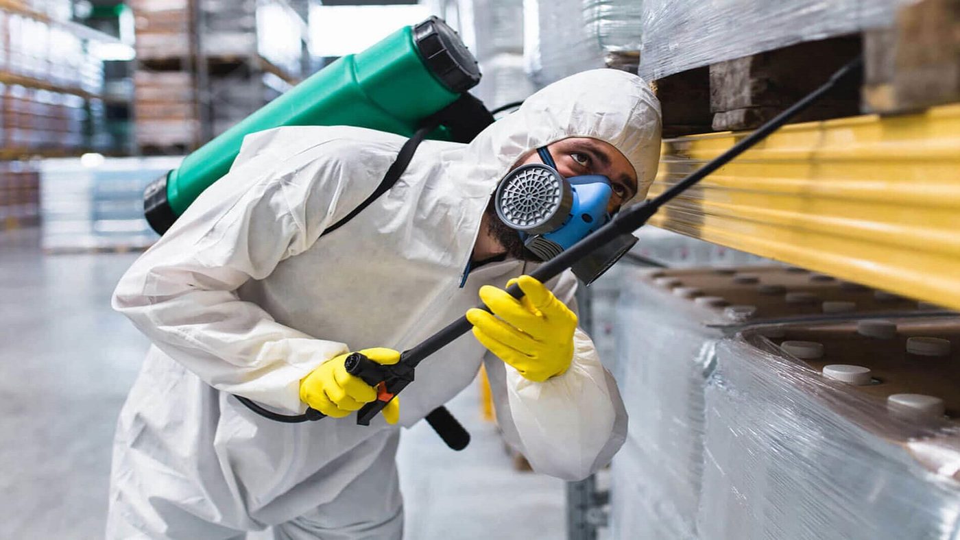 Control estratégico de plagas en depósito industrial — técnico R&B con equipo de protección completo
